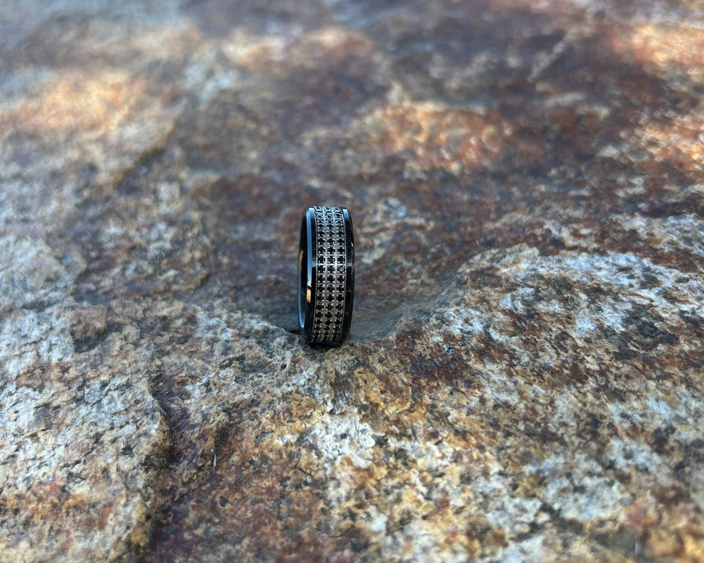 Black ring with rows of black CZ stones on a textured rock