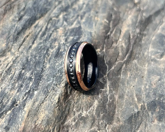 Ring with black band and rose gold accents on a textured stone surface