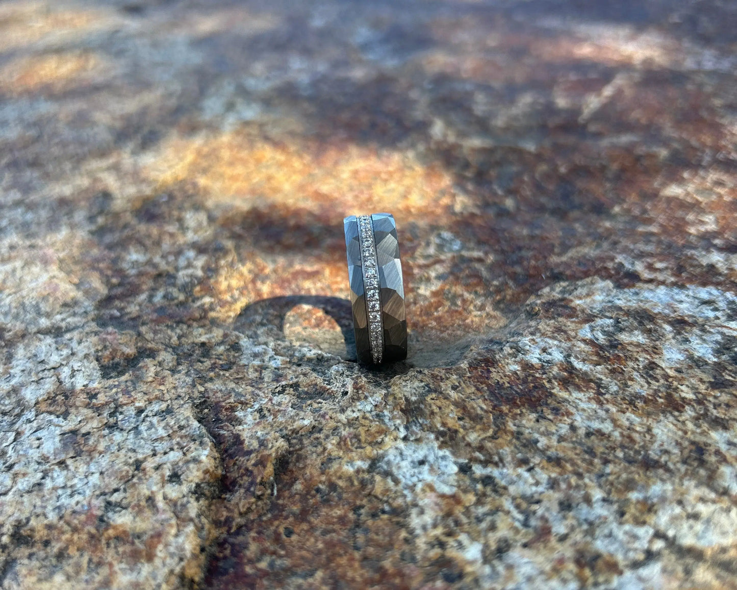 Silver ring with CZ's and hammer accents on a textured rock surface