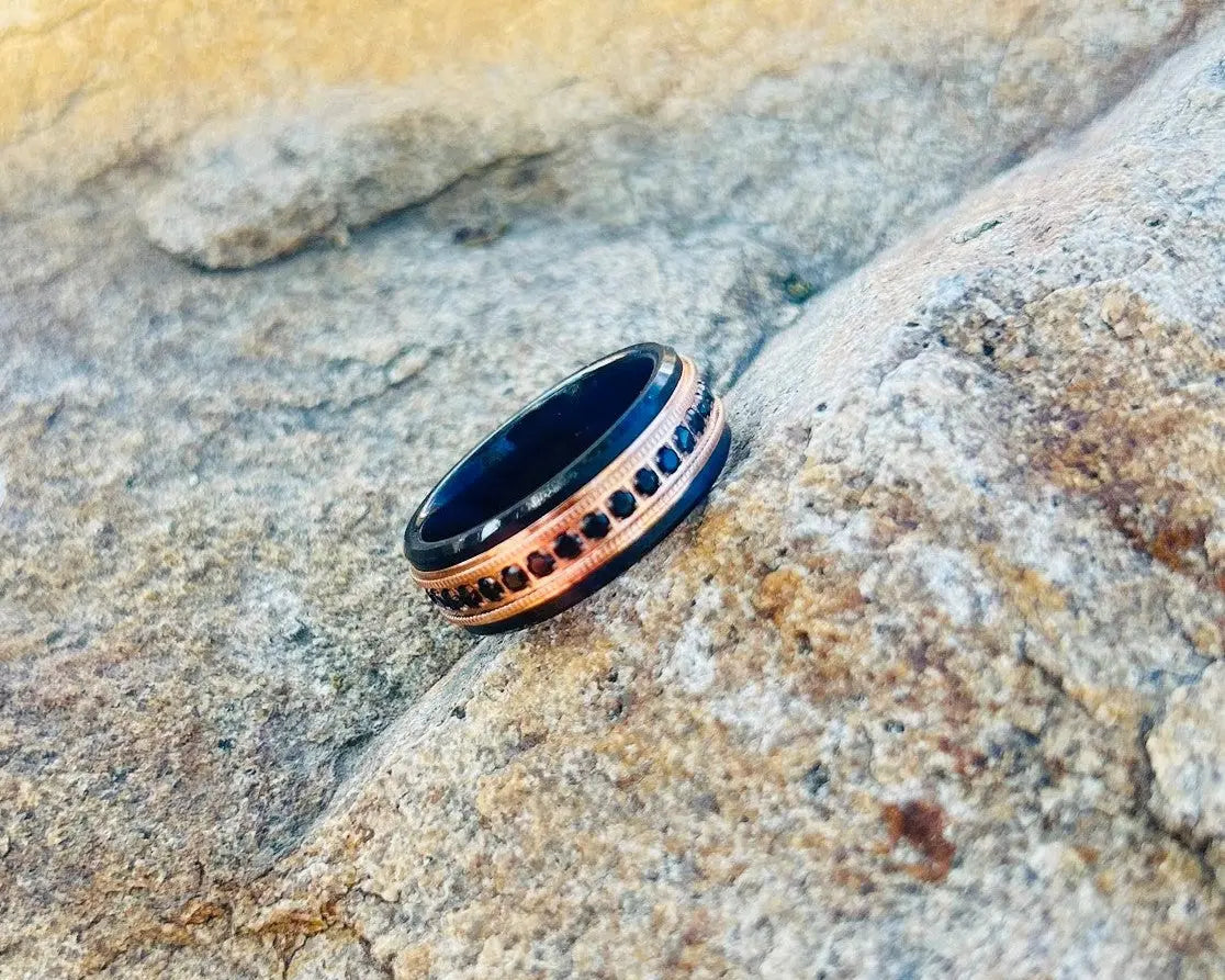 Ring with black and rose gold design on a textured stone surface