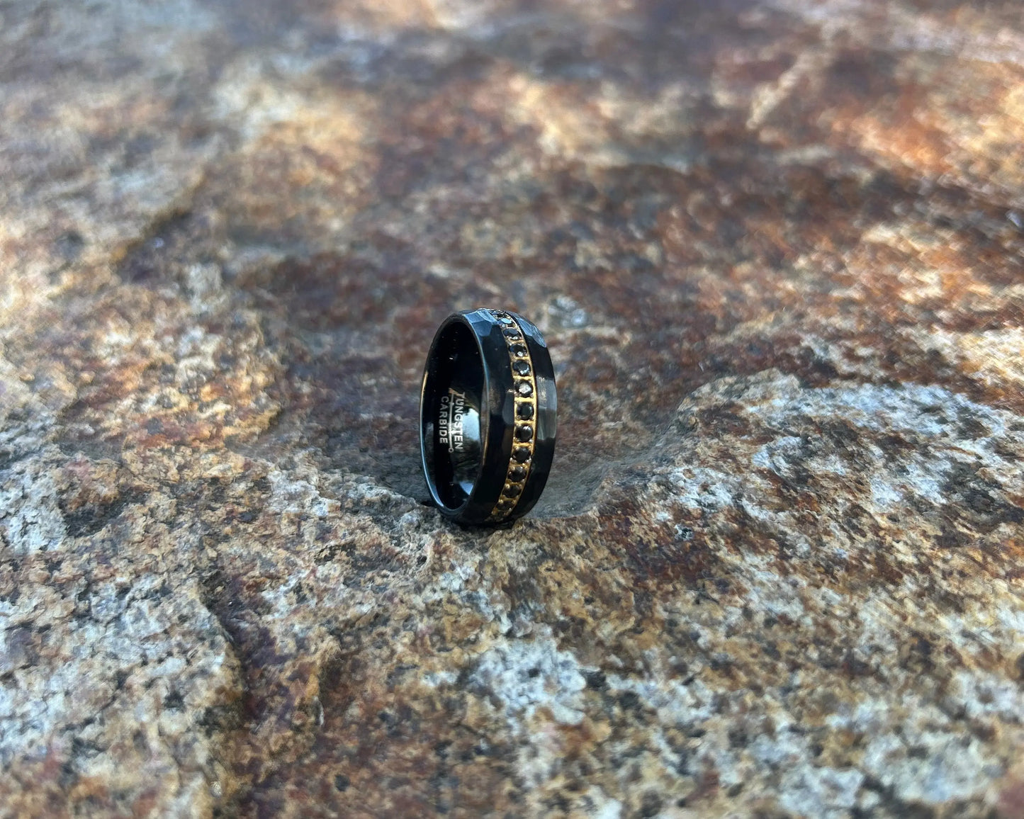 Black ring with decorative band on a textured stone surface