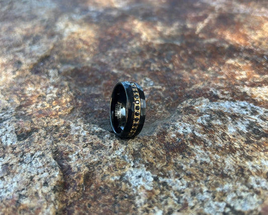 Black ring with decorative band on a textured stone surface