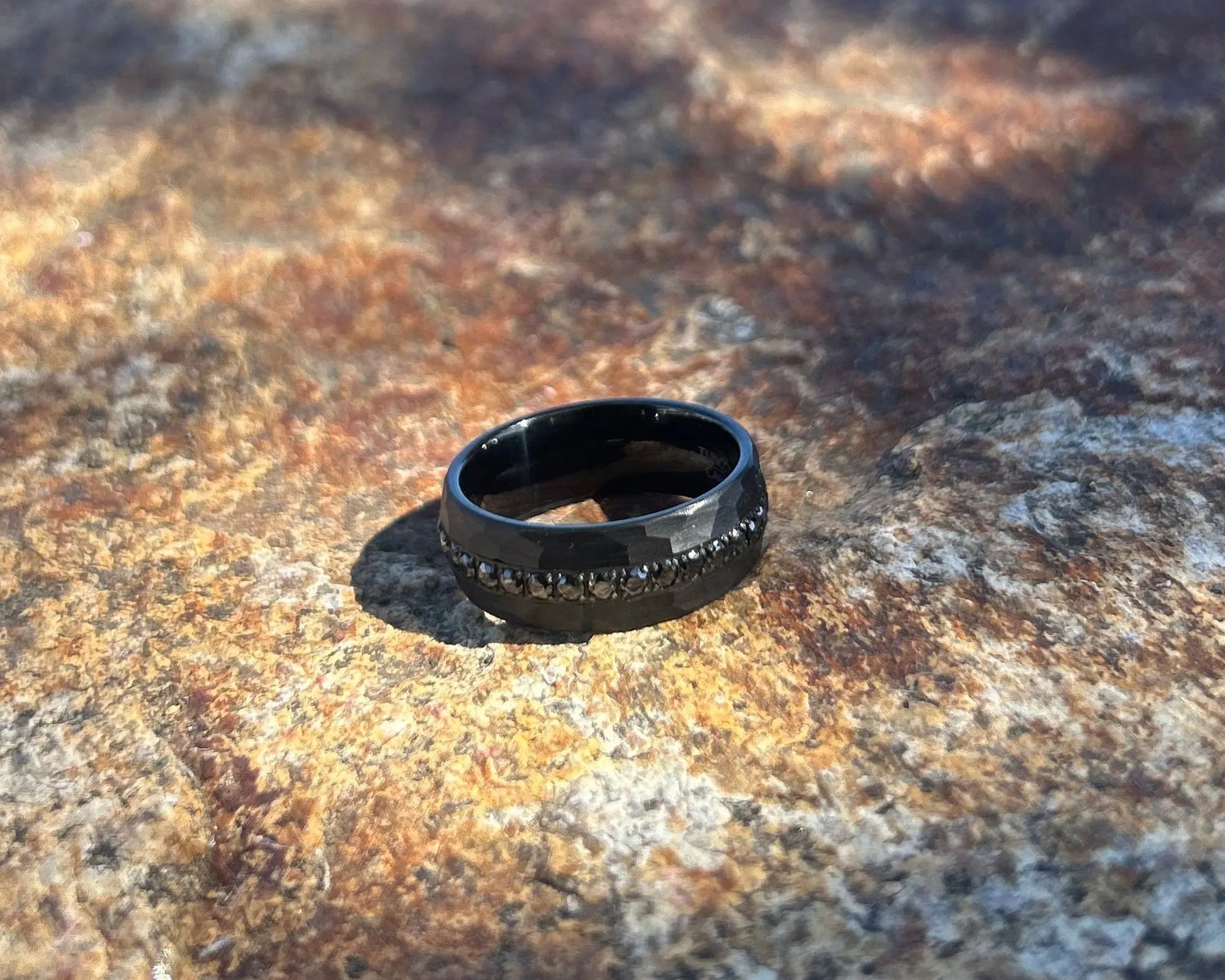 Black ring with hammered design on a textured stone