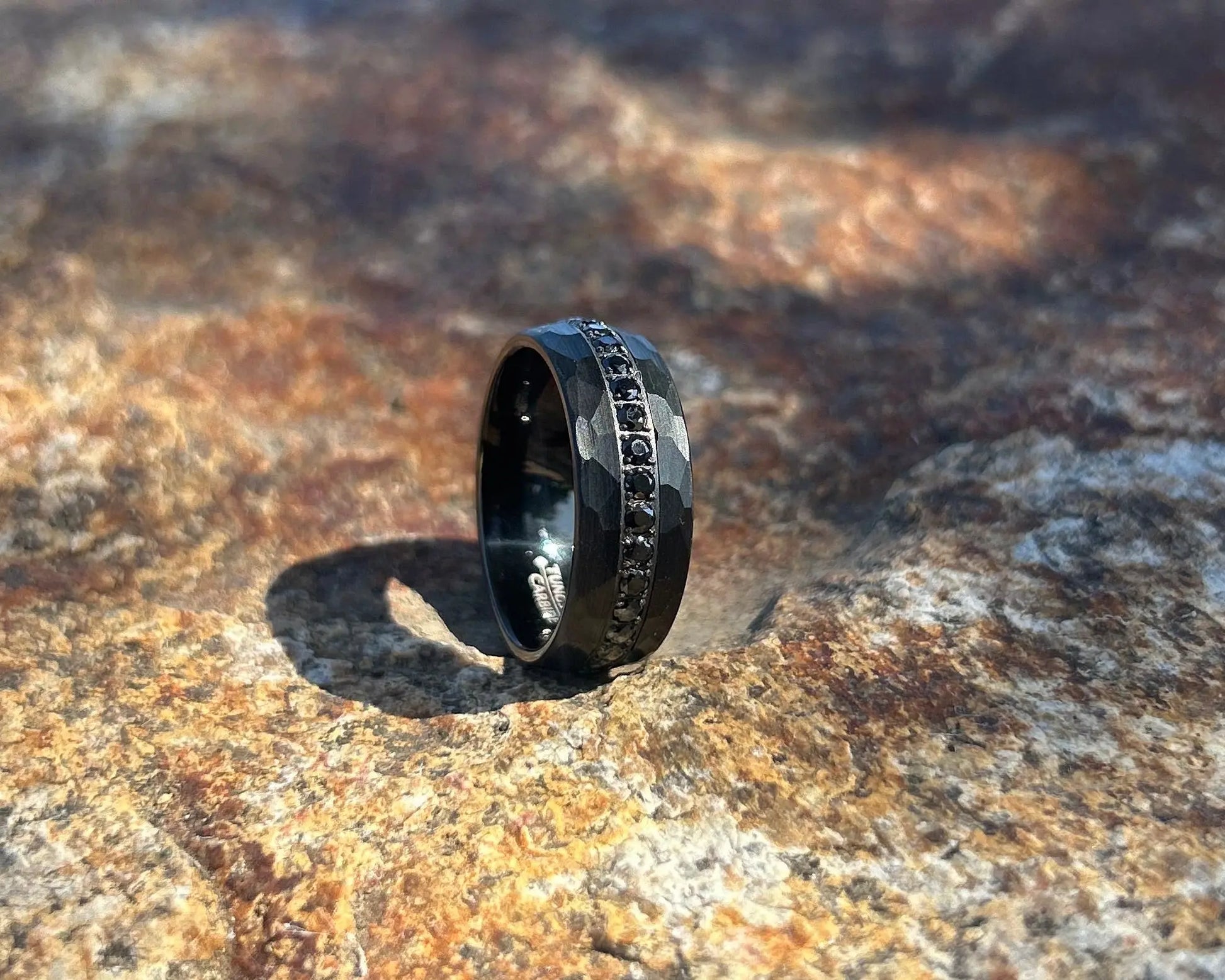 Black ring with hammered design on a textured stone surface