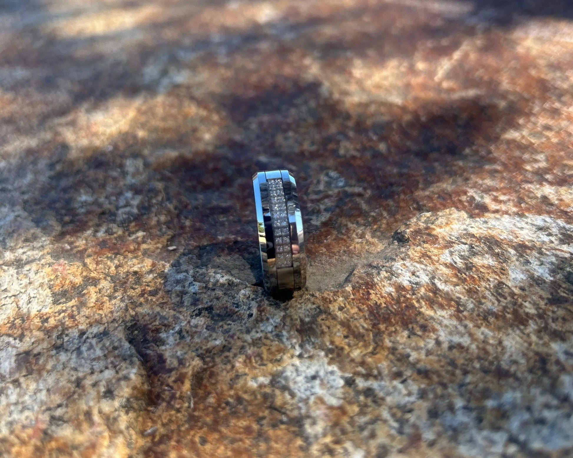 Silver ring with black accents on a textured rock surface