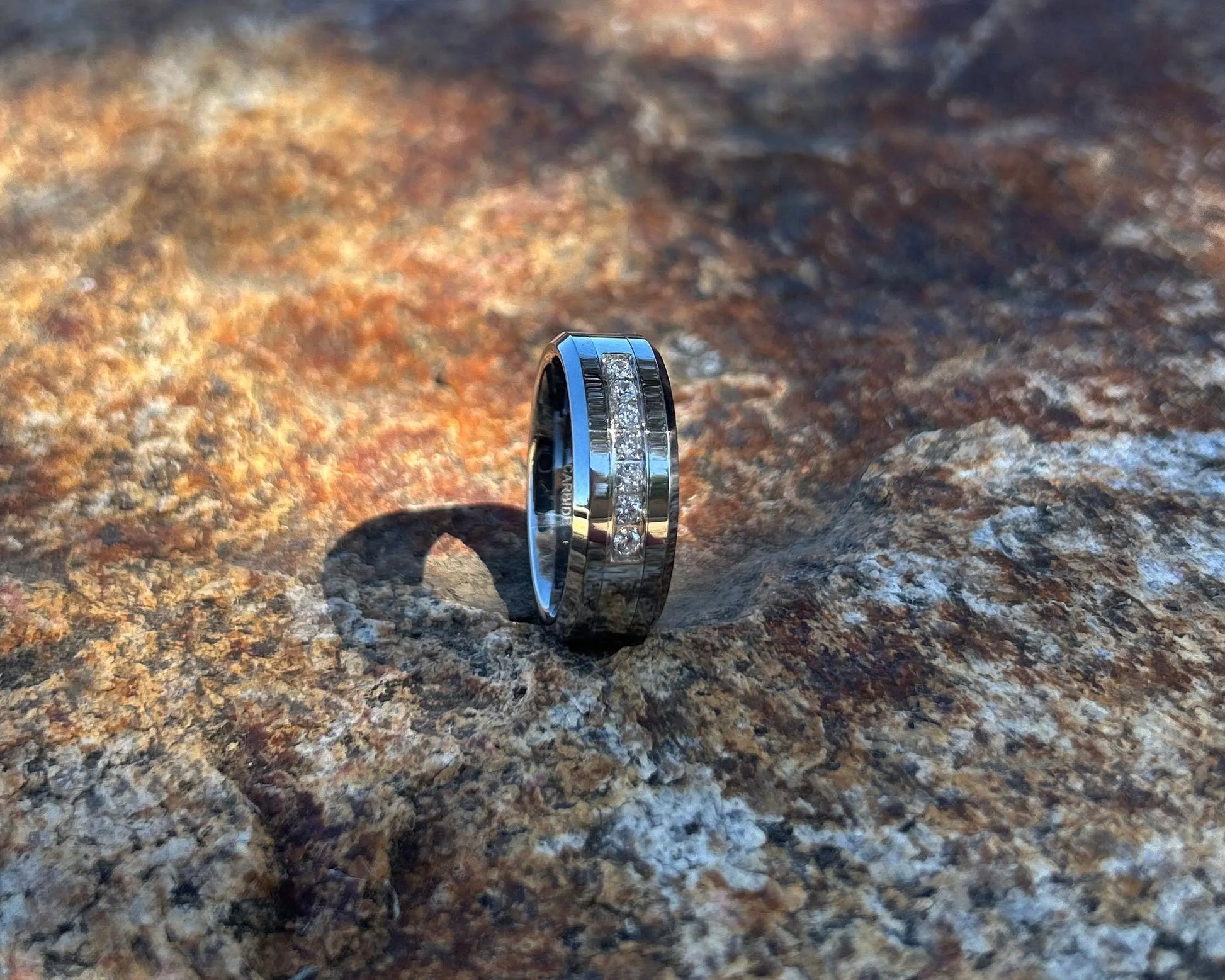Silver ring with CZ channel on a textured stone surface with a blurred natural background